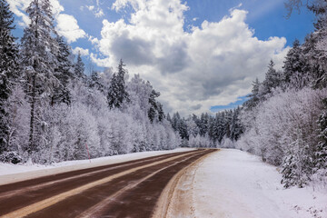 Obraz premium View of highway running alongside winter forest covered in snow, with road markers against backdrop of blue sky with white clouds on frosty day. Sweden.