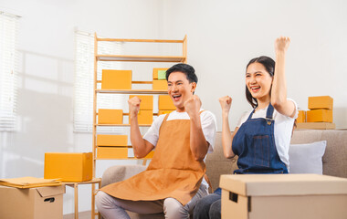 Asian man and woman in aprons celebrate, raising fists in the air with joy, surrounded by moving...