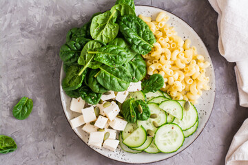 Bowl with pasta, cucumber, cheese and spinach on the table. Top view. Close-up - obrazy, fototapety, plakaty