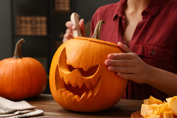 Woman carving pumpkin for Halloween at wooden table indoors, closeup