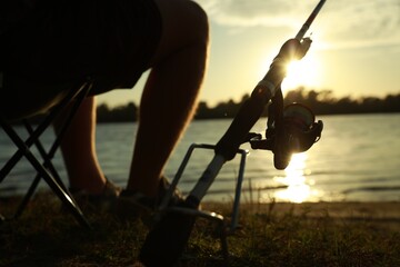 Fisherman with rod sitting on folding chair and fishing at riverside, closeup