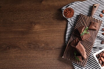 Pieces of tasty milk chocolate, cocoa beans, powder and mint on wooden table, top view. Space for...