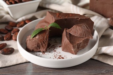 Pieces of tasty milk chocolate, cocoa beans, powder and mint on wooden table