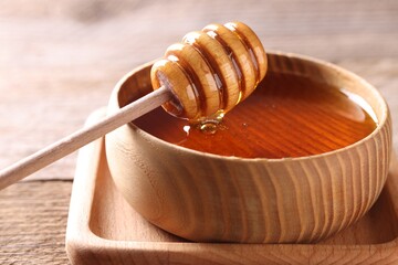 Delicious honey in bowl and dipper on wooden table, closeup