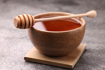 Delicious honey in bowl and dipper on grey textured table, closeup