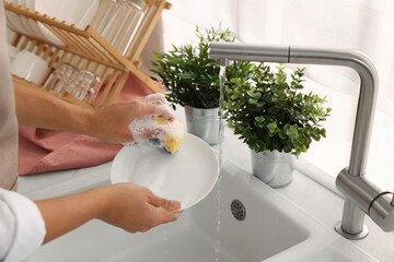 Woman washing plate at sink in kitchen, closeup