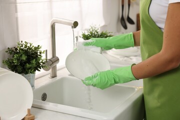 Woman washing plate at sink in kitchen, closeup
