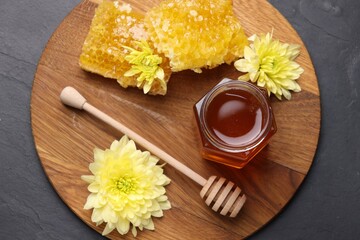 Sweet honey in jar, dipper, chrysanthemum flowers and pieces of honeycomb on grey textured table, top view