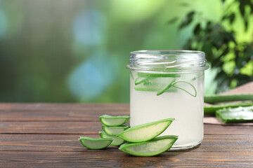 Fresh aloe juice in jar and cut leaves on wooden table outdoors, space for text