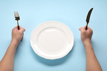 Man with cutlery and empty plate at light blue table, closeup