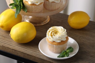 Delicious lemon cupcakes with white cream, mint and lemons on wooden table, closeup