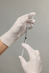 Doctor filling syringe with medication from glass vial on grey background, closeup