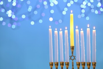 Hanukkah celebration. Menorah with burning candles on light blue background with blurred lights, space for text