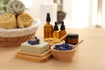 Soap bar, dry flowers, bottles of essential oils, jar with cream and towels on wooden table indoors. Spa time