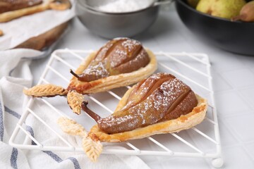 Delicious pears baked in puff pastry with powdered sugar on white tiled table, closeup