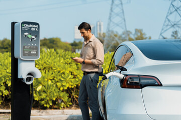 Man pay for electricity with smartphone while recharge EV car battery at charging station connected...
