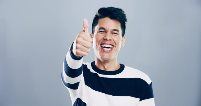Smile, studio face and man thumbs up sign for thank you, support feedback or vote opinion, agreement or winning motivation. Portrait, laughing and male model with emoji like icon on grey background