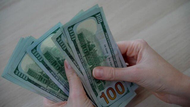 Close-up of unrecognizable female hands counting a stack of American hundred dollar bills. Receiving kickbacks and bribes. The dominance of American dollars over other world currencies.