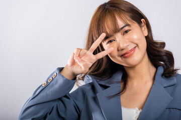 In a studio shot on a white background, an Asian woman radiates positivity by forming victory and...