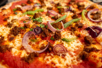 Close up of a pizza in a restaurant with cheese, tomato, onion, pepper and beef