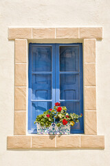 Fototapeta na wymiar Blue window with brick frame with red flowers in the Maltese alleys