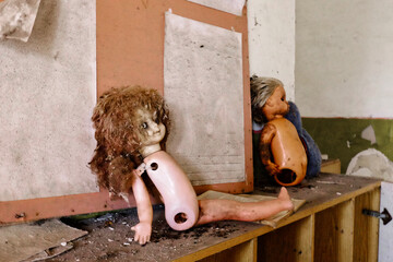 The image shows a doll with a brown wig and a white body, missing its legs, sitting on a wooden...