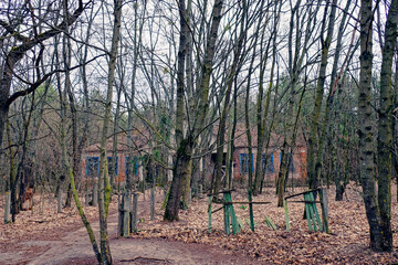 An abandoned one-story building in the woods. The facade of an abandoned kindergarten in the Chernobyl radioactive zone. Autumn foliage on the ground. Trees in front of an old abandoned house.