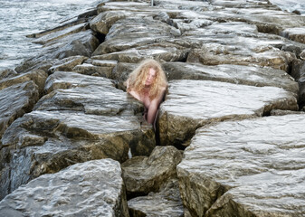 portrait of sexy, mature red haired woman with long curly red hair crouches between marble stone blocks texture of breakwater at Marinella di Sarzana, Carrara, tuscany, italy