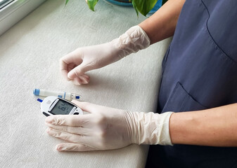 Close up shot of the glucometr instrument on the white surface. Nurse helping patient to check sugar level. Healthcare - obrazy, fototapety, plakaty