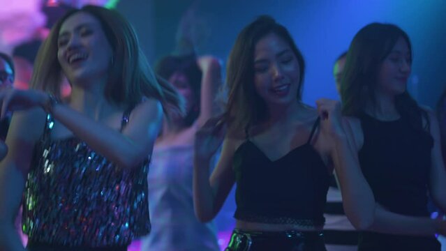 Happy fun Asian thai people dance in night club. Group of Sexy young woman people dancing and holding champagne glass in night club. Nightlife and disco dance party concept. Fun music festival