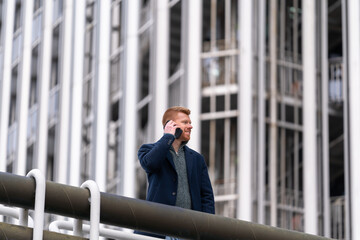 Red-haired businessman, engaged in a phone call on a terrace, exuding professionalism with a panoramic view in the business environment.