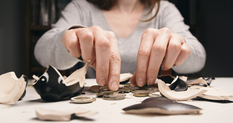 A Caucasian woman collecting coins from a broken piggy bank