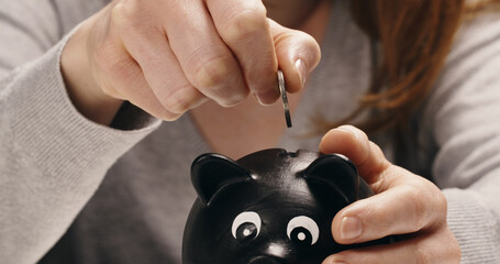 A smiling Caucasian woman puts coins in a piggy bank
