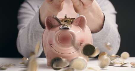 A Caucasian woman pours a lot of Euro coins over a piggy bank