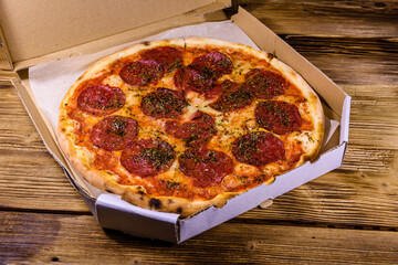 Pizza with salami sausage and parmesan cheese in cardboard box on a wooden table