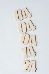 the numbers 84, 94, 04, 14, and 24 in wooden digits on plain white paper