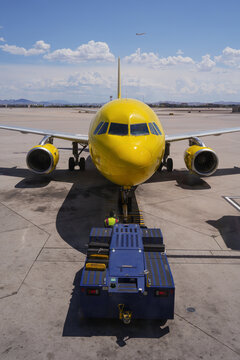 Yellow airplane and other vehicles against a vibrant sky at the airport