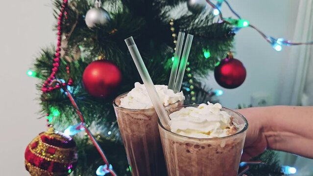 New Year Christmas clatter glasses of hot chocolate cocoa with cream and straws Christmas tree bright red toys lights family gatherings celebration drinking hot drink in evening near tree