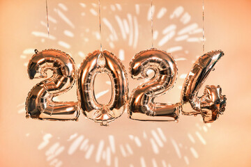 Silber foil balloons in numbers shape 2024 hanging against peach wall with fireworks projection. New Year holidays. Color of the year fuzz peach