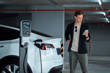 Young man travel with EV electric car to shopping center parking lot charging in downtown city...