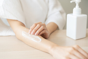 Health care, beauty smile pretty asian young woman in bathrobe, towel after shower bath at home, hand applying, putting moisturizer on her arm. Skin body cream moisturizing lotion, routine in morning.