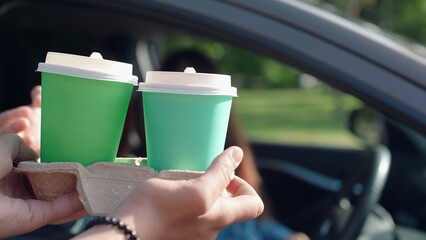 Woman driving, delivery of drinks to car. Fast food concept, hot tea delivery through car window. Delicious coffee for travelers by car. Food for driver, passenger to eat on road. Buying coffee in car - obrazy, fototapety, plakaty