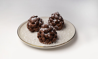 Christmas tree cone-shaped cookies with chocolate flakes with powdered sugar, a delightful homemade dessert for the New Year. These chocolate pine cone-shaped shortbread cookies with sweet snow.	
