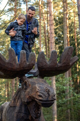 Fototapeta na wymiar A father with his little boy on a large wooden elk antlers in the forest, tree tops in the background.