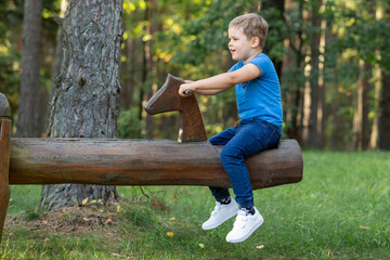 Full length shot, of a smiling boy sitting alone on a seesaw in green forest background