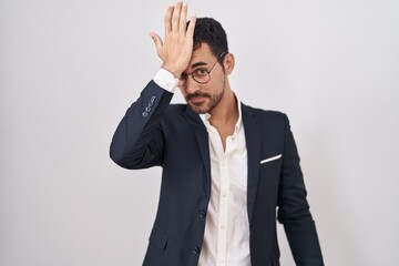 Handsome business hispanic man standing over white background surprised with hand on head for...