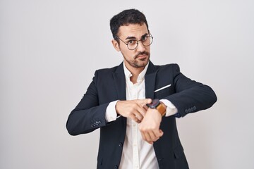 Handsome business hispanic man standing over white background in hurry pointing to watch time,...