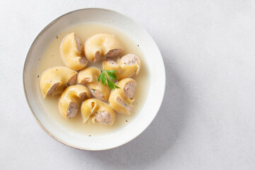 Traditional Catalan Christmas dish Escudella in white plate on table, stuffed pasta in meat broth, top view