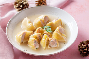 Traditional Catalan Christmas dish Escudella in white plate on pink table, stuffed pasta in meat broth, top view
