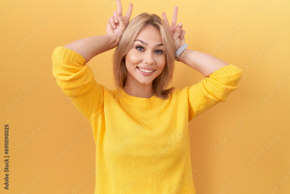 Poster young caucasian woman wearing yellow sweater posing funny and crazy with fingers on head as bunny ea